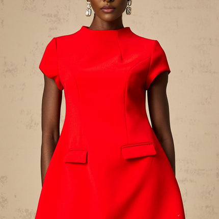 A woman wearing a bright red mini dress with cap sleeves standing against a plain background