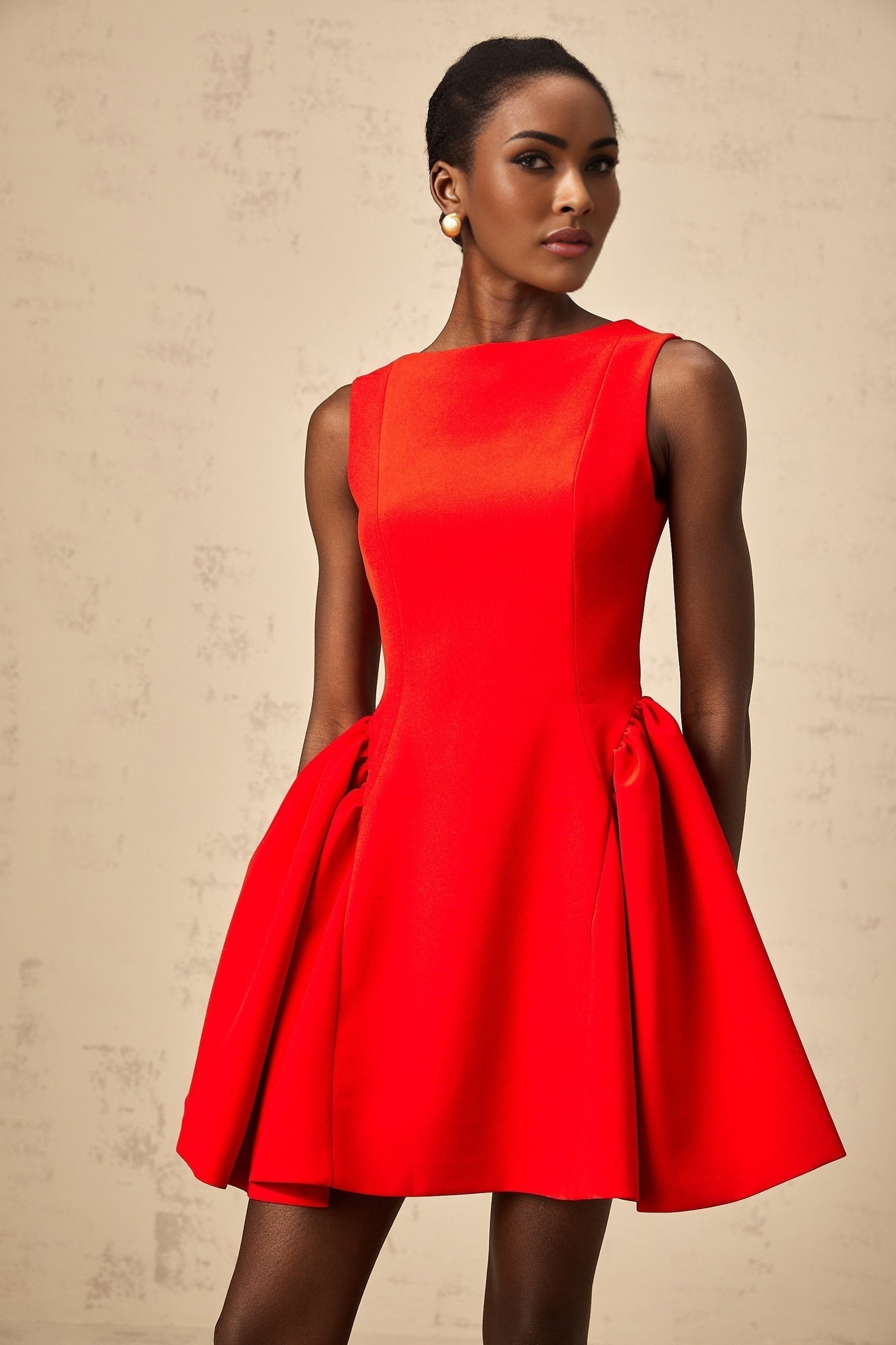 A woman wearing a bright red sleeveless mini dress with a flared skirt standing against a plain background