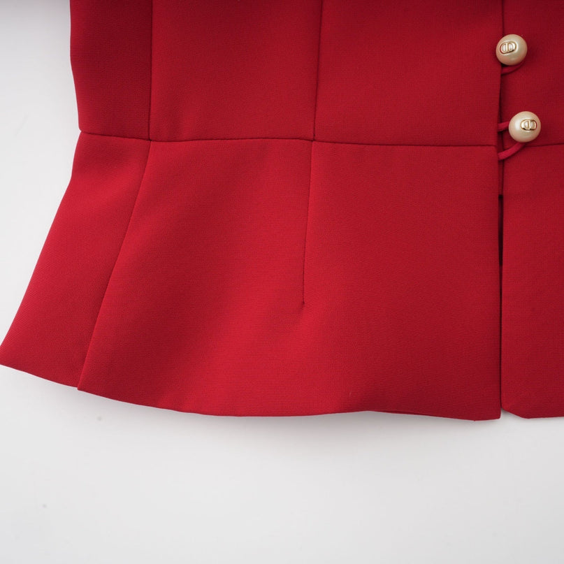A woman wearing a bright red twopiece outfit consisting of a pleated blouse and matching pleated skirt standing against a plain background