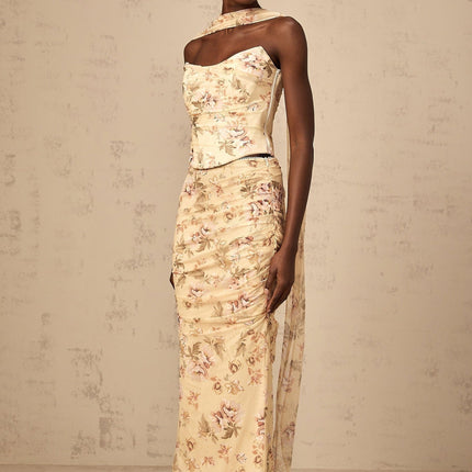 A woman wearing a bright yellow floral print matching set consisting of a fitted top and skirt standing against a plain background