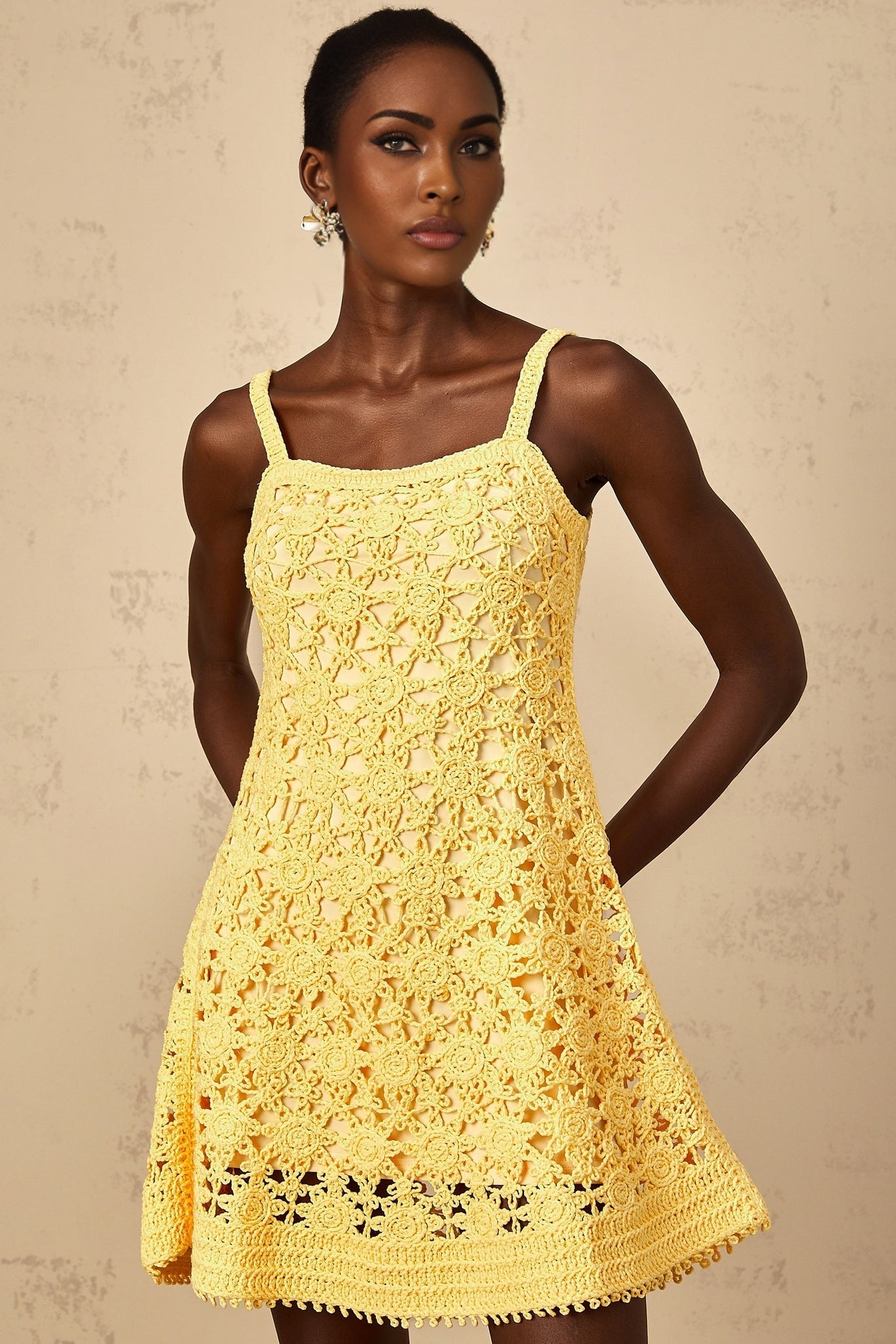 A woman wearing a bright yellow mini dress with a flared skirt and crochet knit pattern standing against a plain background