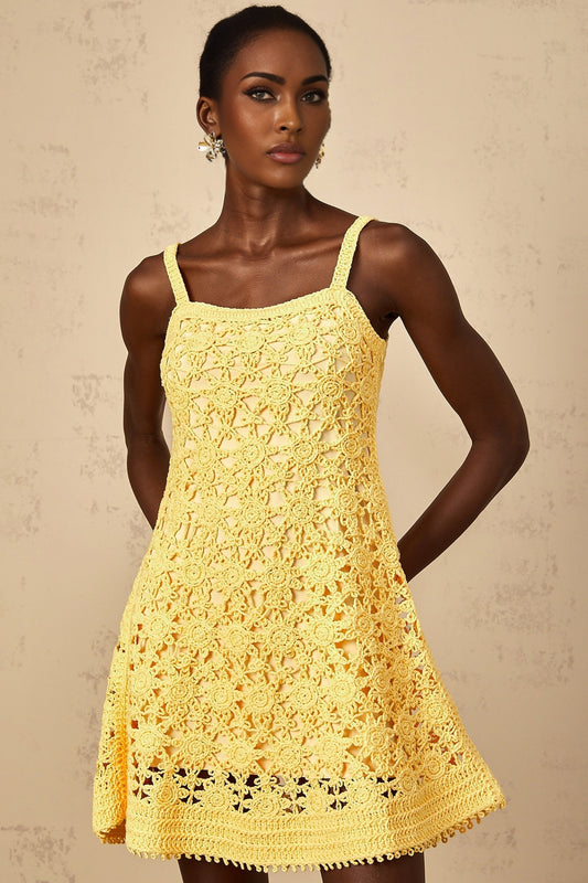 A woman wearing a bright yellow mini dress with a flared skirt and crochet knit pattern standing against a plain background