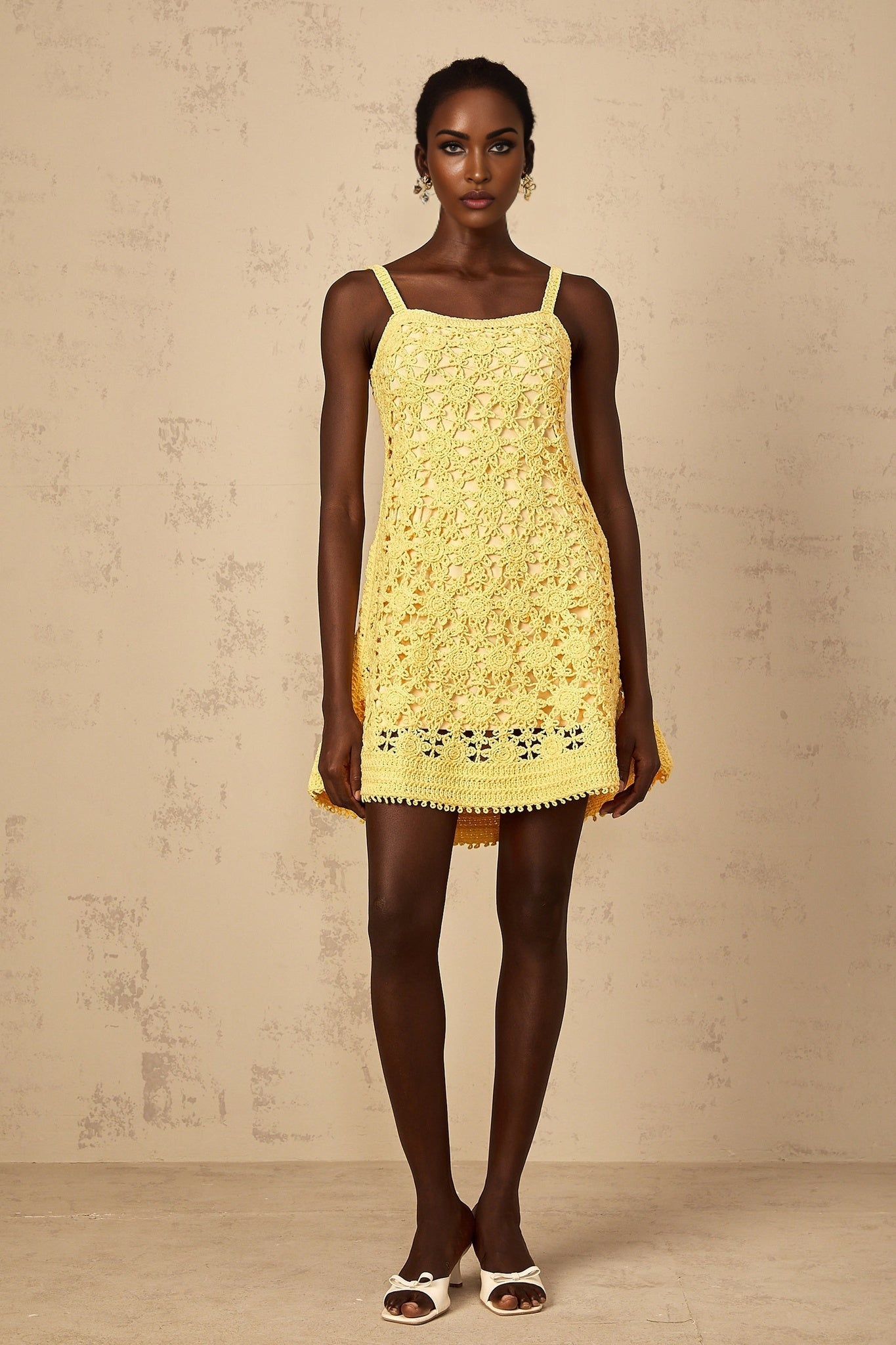 A woman wearing a bright yellow mini dress with a flared skirt and crochet knit pattern standing against a plain background
