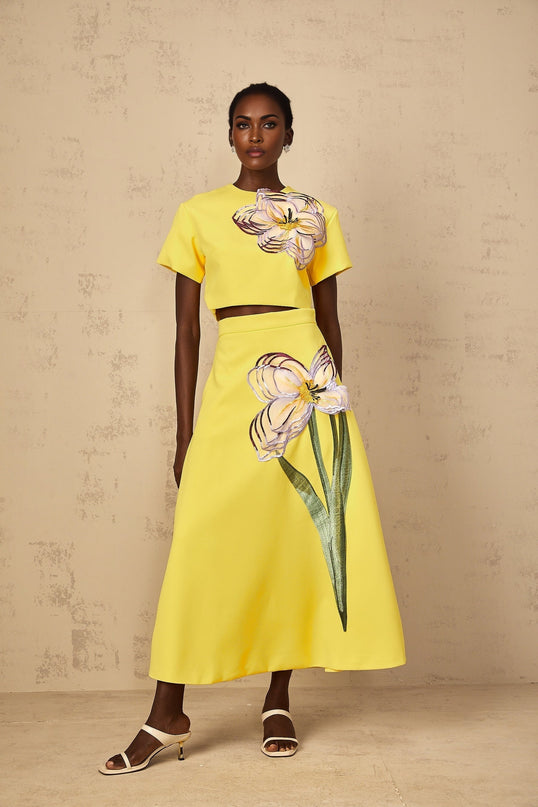 A woman wearing a bright yellow twopiece outfit featuring sequin floral embroidery on both the top and bottom matching set