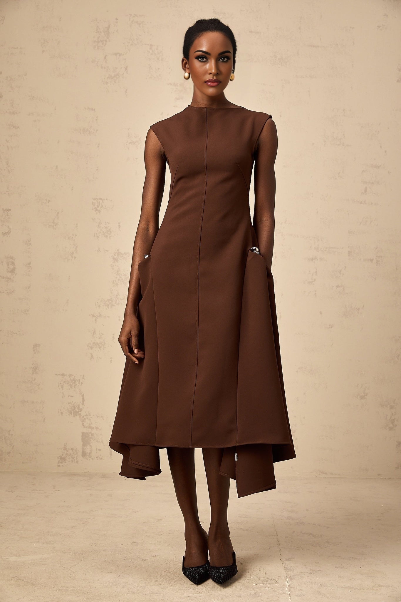 A woman wearing a brown asymmetrical midi dress with a flowing silhouette and unique design details