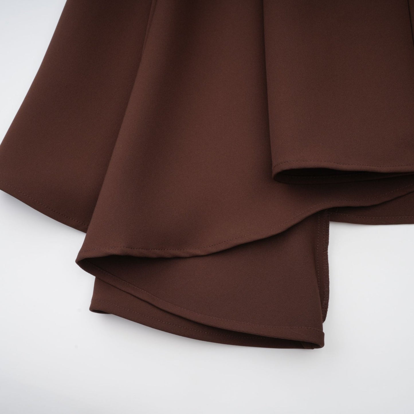 A woman wearing a brown asymmetrical midi dress with a flowing skirt and one shoulder design