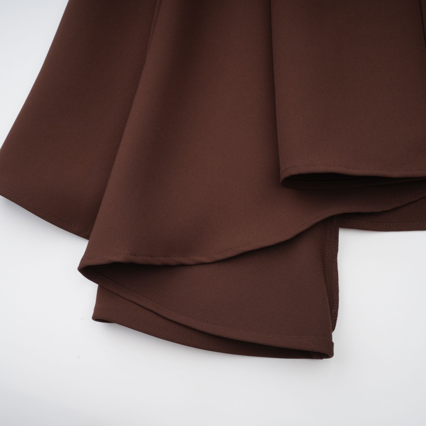 A woman wearing a brown asymmetrical midi dress with a flowing skirt and one shoulder design