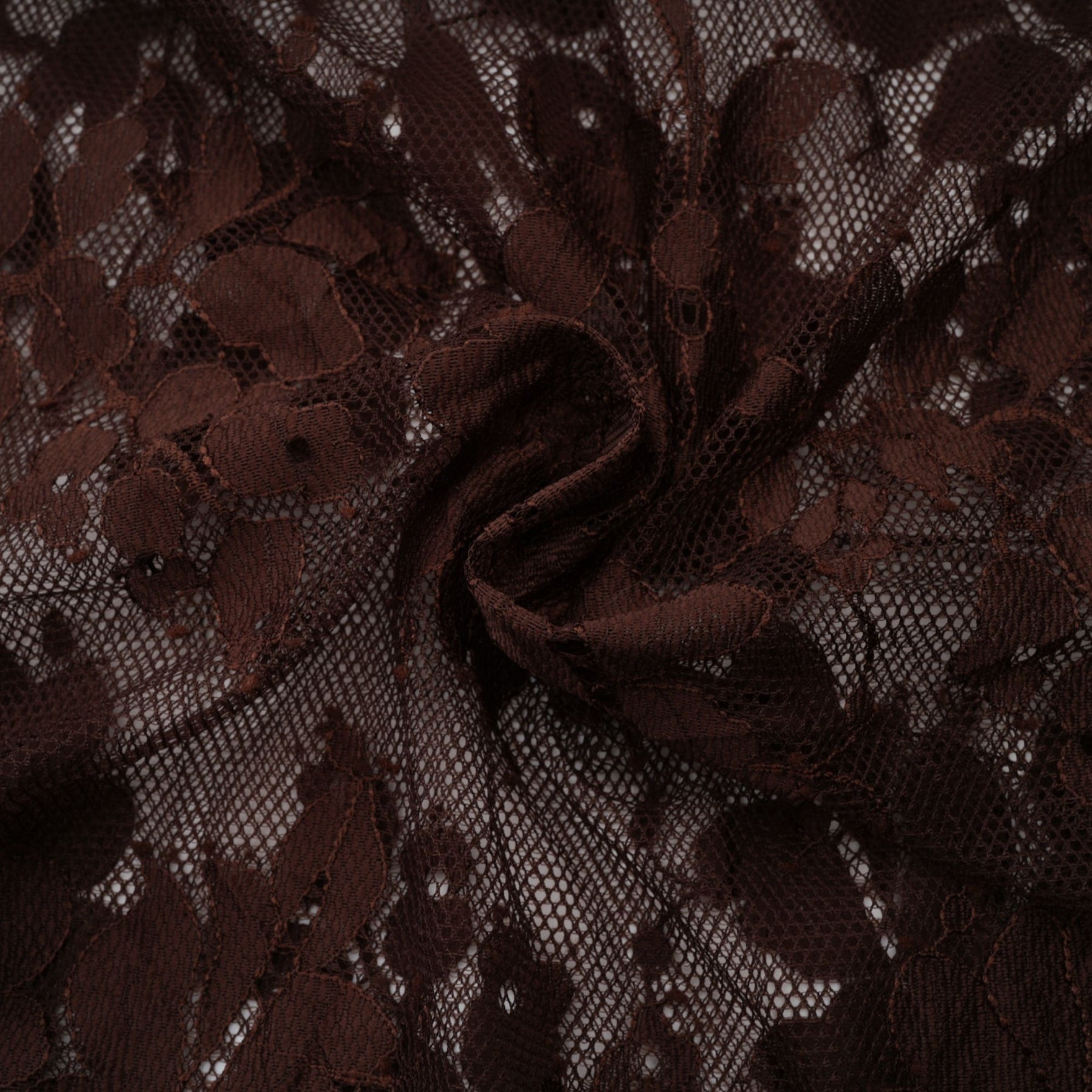 A woman wearing a brown flared midi dress made of delicate chantilly lace named Sylvie The dress features a fitted bodice and flows into an elegant flared skirt