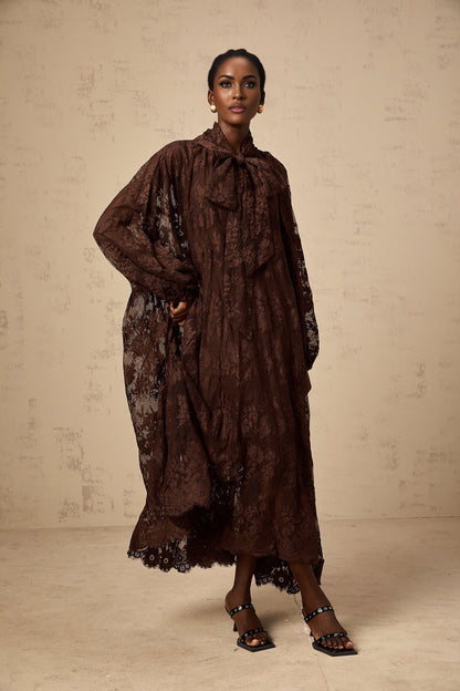 A woman wearing a brown lace midi dress with a flared skirt and delicate chantilly lace pattern The dress has a fitted bodice and falls to mid calf length