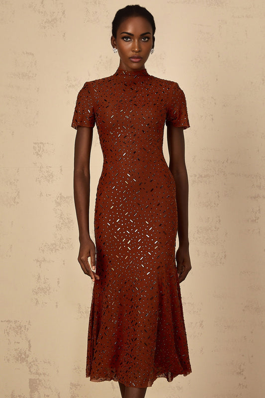 A woman wearing a brown midi dress with a flared tulle skirt and embellished details standing in a neutral pose