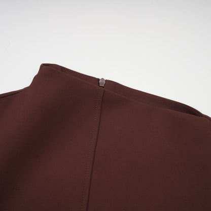 A woman wearing a brown mini dress with an asymmetric neckline and puff sleeves standing against a plain background
