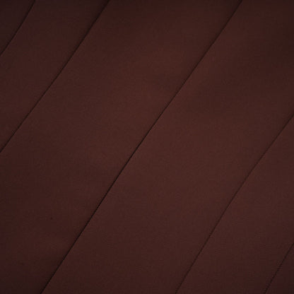A woman wearing a brown mini dress with an asymmetric neckline and puffed sleeves standing against a plain background