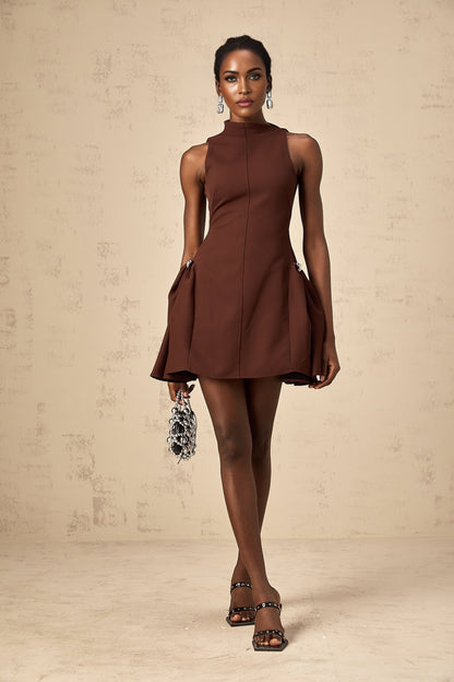 A woman wearing a brown mini dress with an asymmetric neckline and puffed sleeves standing against a plain background