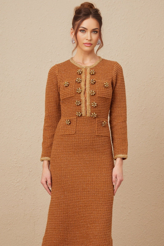 A woman wearing a brown tweed dress with braided edges standing in a neutral setting