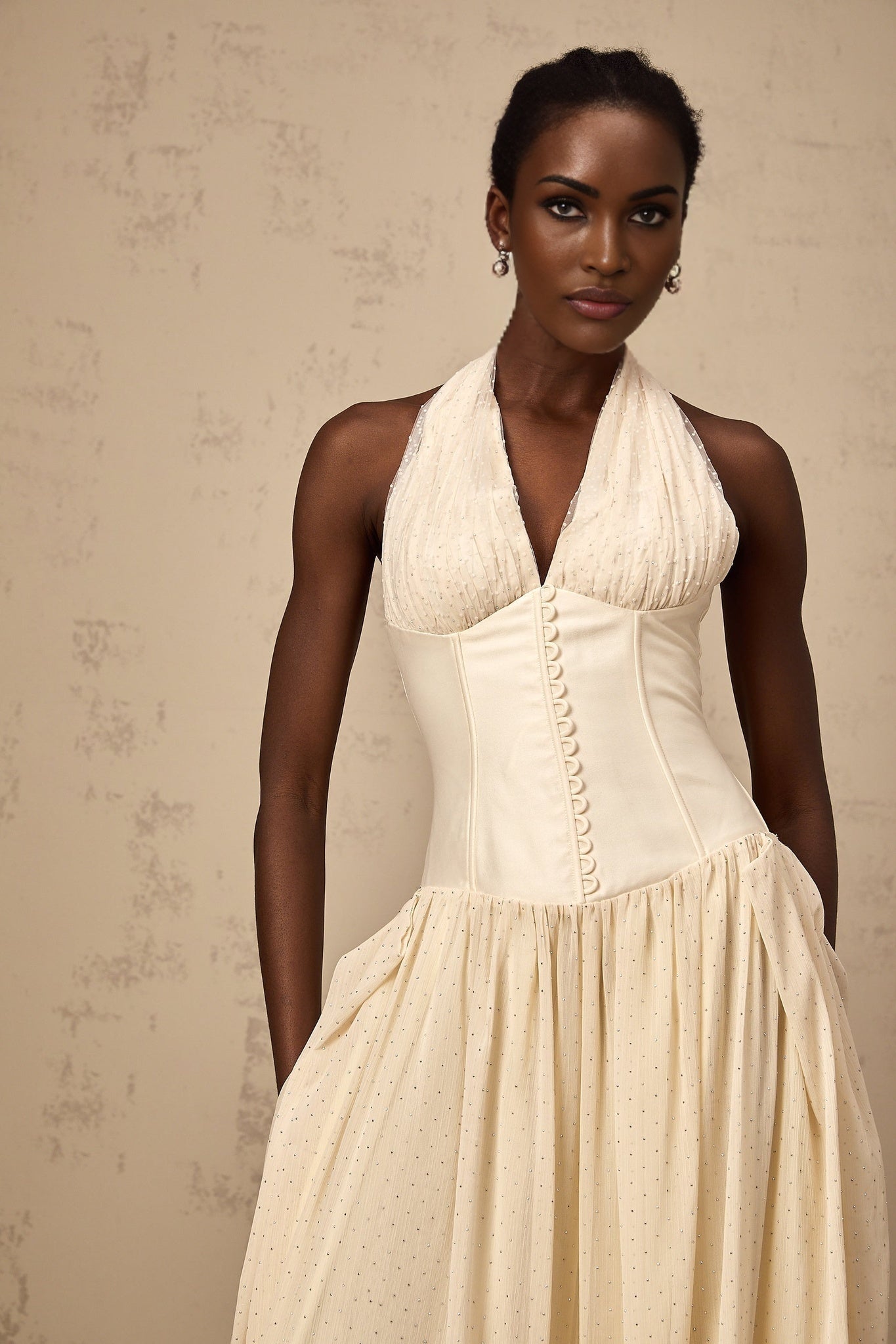 A woman wearing a Charlotte halterneck tulle midi dress in soft pastel color standing against a plain background