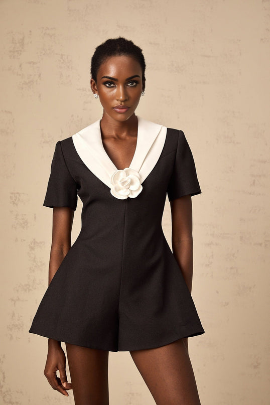 A woman wearing a colorblocked jumpsuit with floral appliques standing in a casual pose against a plain background