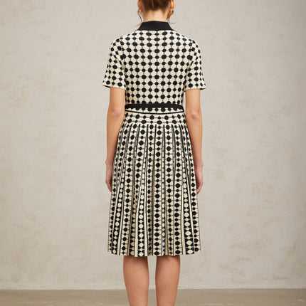 A woman wearing a colorblocked midi dress with polka dot pattern in contrasting colors standing against a plain background