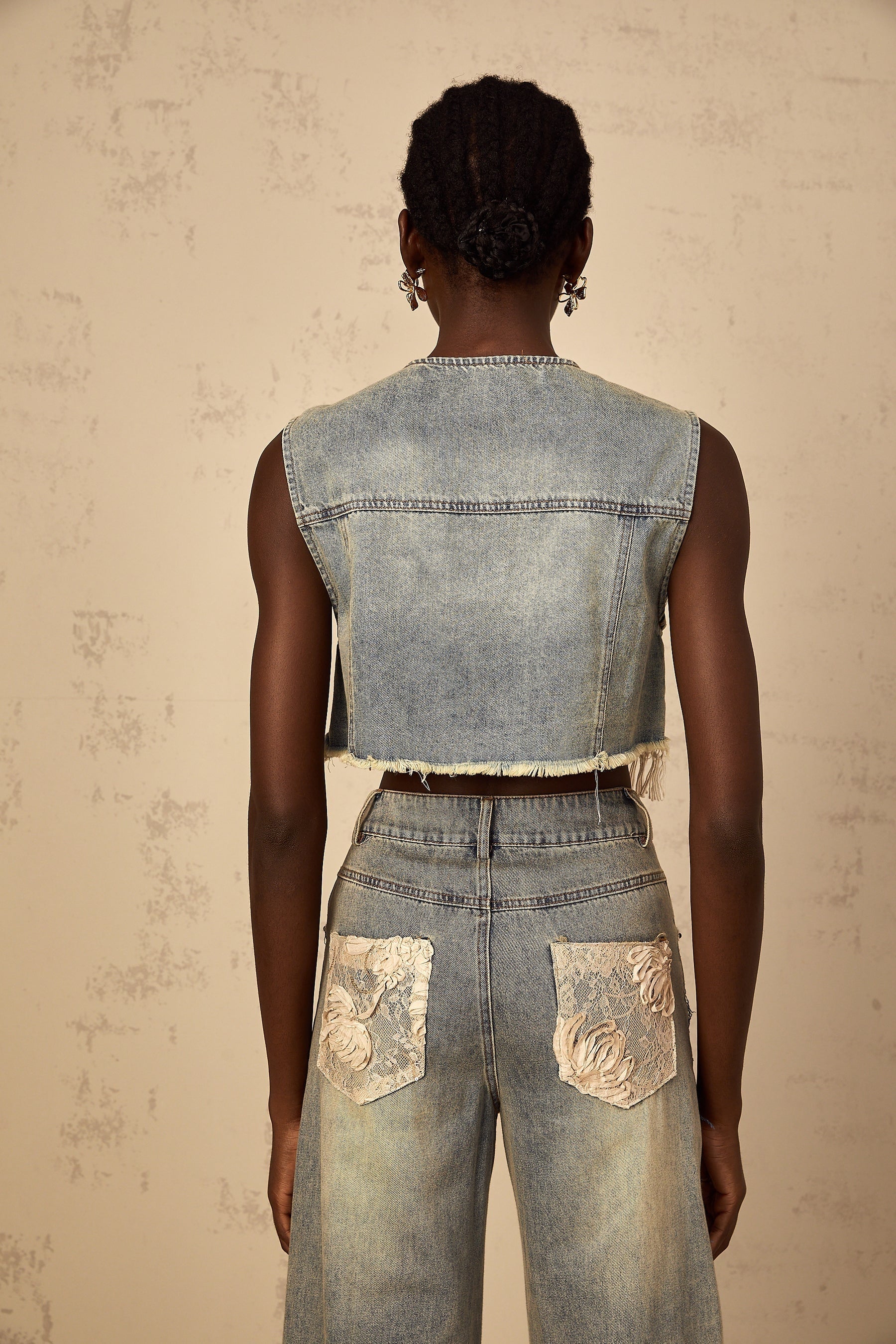 A woman wearing a cropped denim top with blue lace panelling and short sleeves The top has a fitted silhouette and ends above the waist