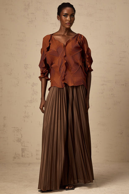 A woman wearing a demi brown matching set consisting of a creased top and skirt standing against a plain background