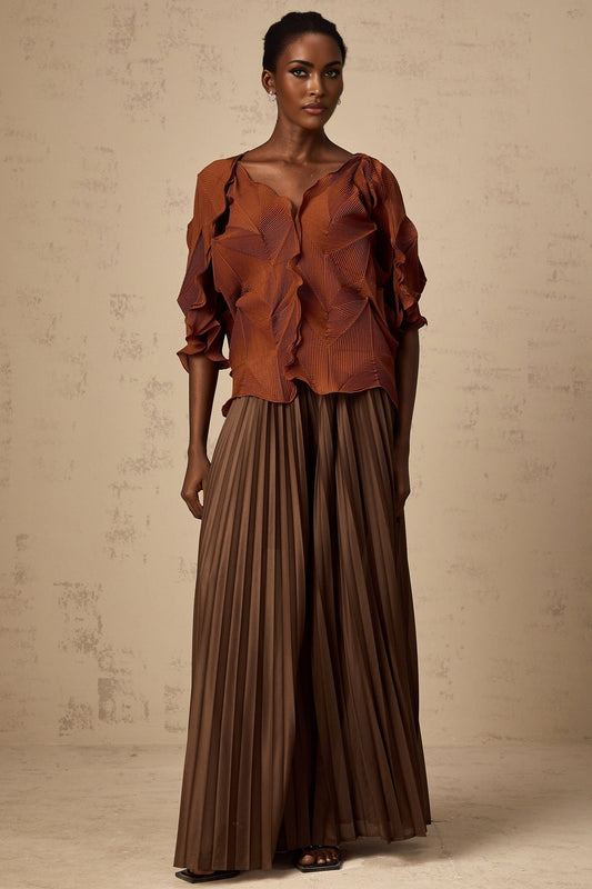 A woman wearing a demi brown matching set consisting of a creased top and skirt standing against a plain background