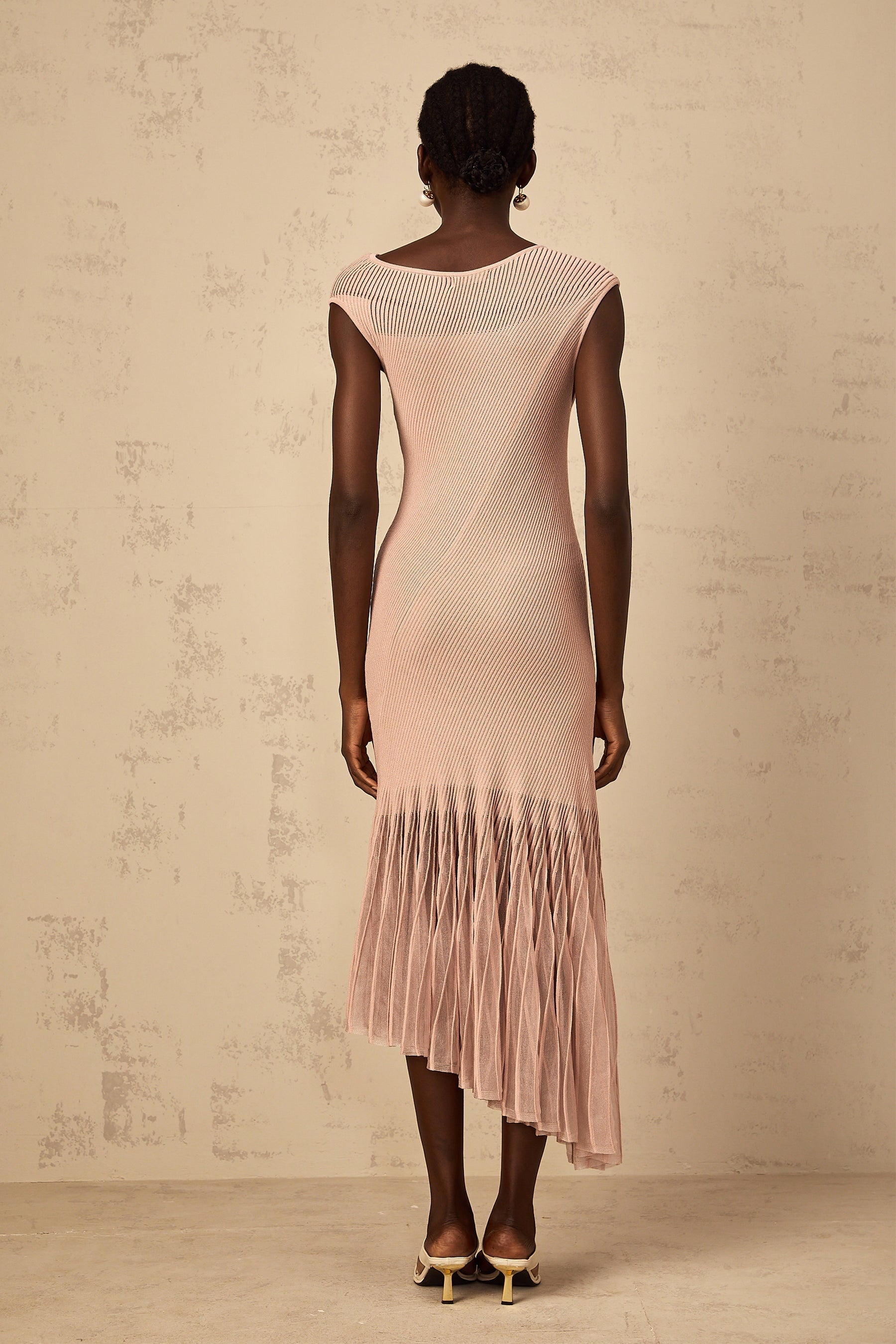 A woman wearing a dusty pink midi dress with a ribbed knit bodice and flowing tulle skirt panel standing in a relaxed pose