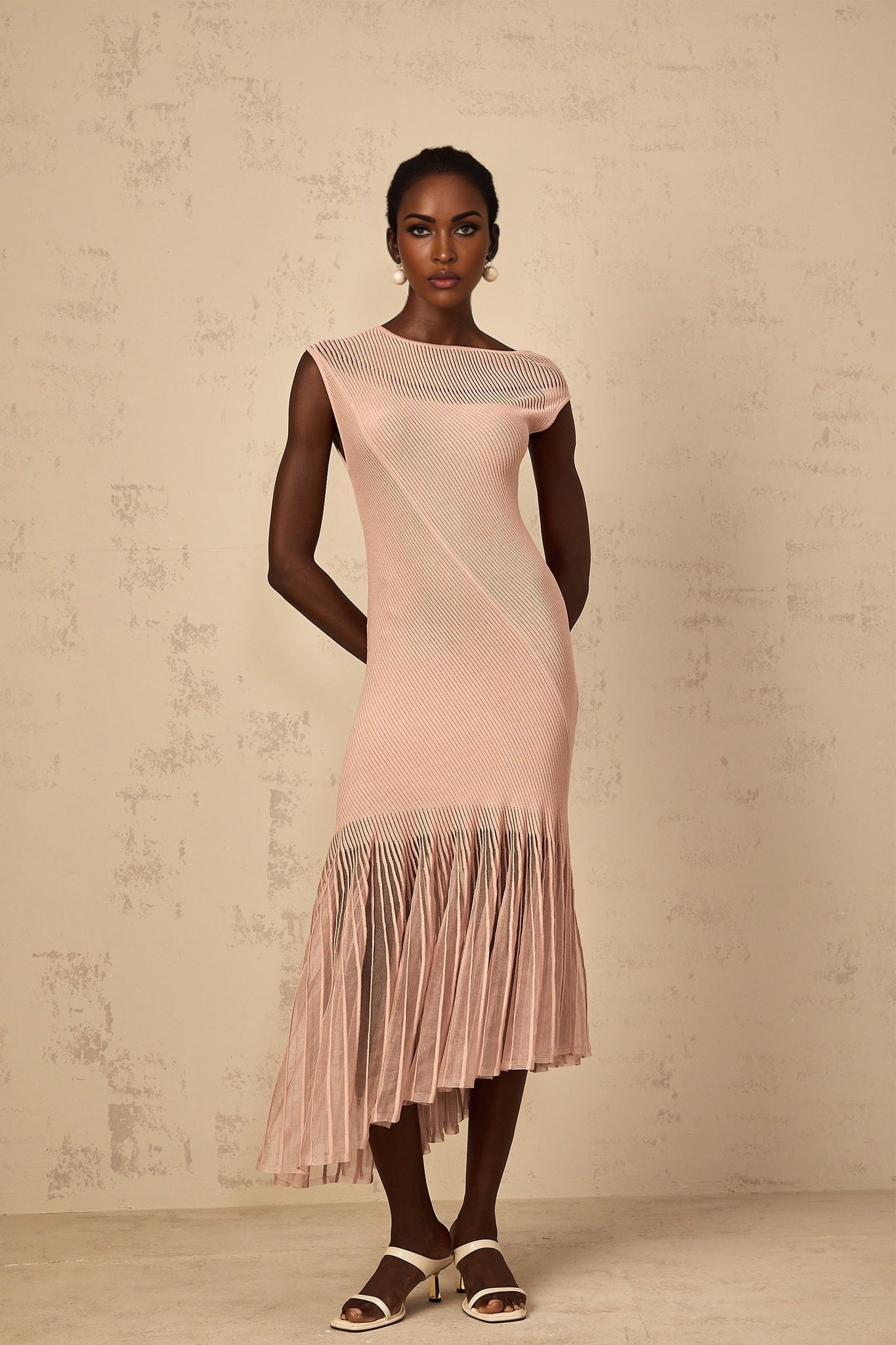 A woman wearing a dusty pink midi dress with a ribbed knit bodice and tulle panel skirt standing in a neutral background