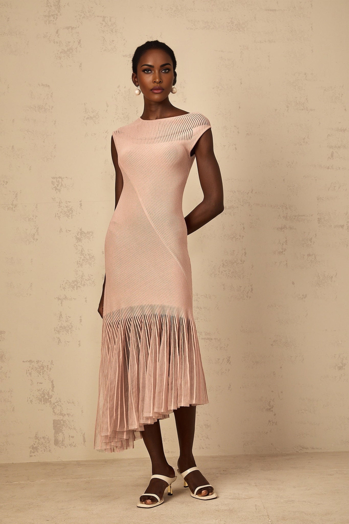 A woman wearing a dusty pink midi dress with a ribbed knit body and sheer tulle panel details standing in a neutral background