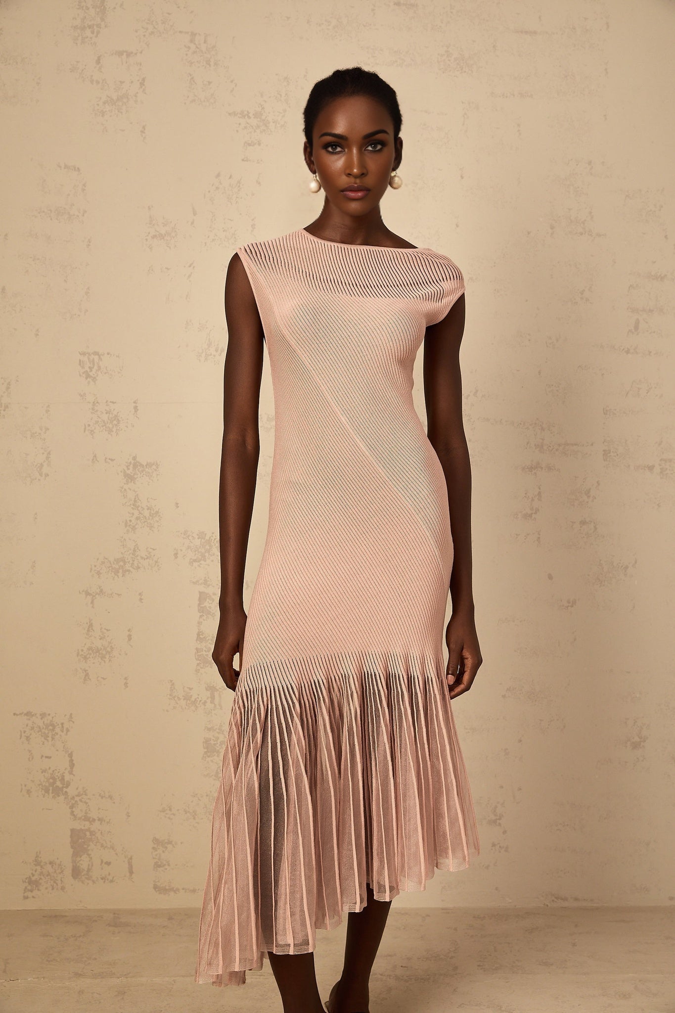 A woman wearing a dusty pink midi dress with a ribbed knit body and tulle panel details standing in a relaxed pose