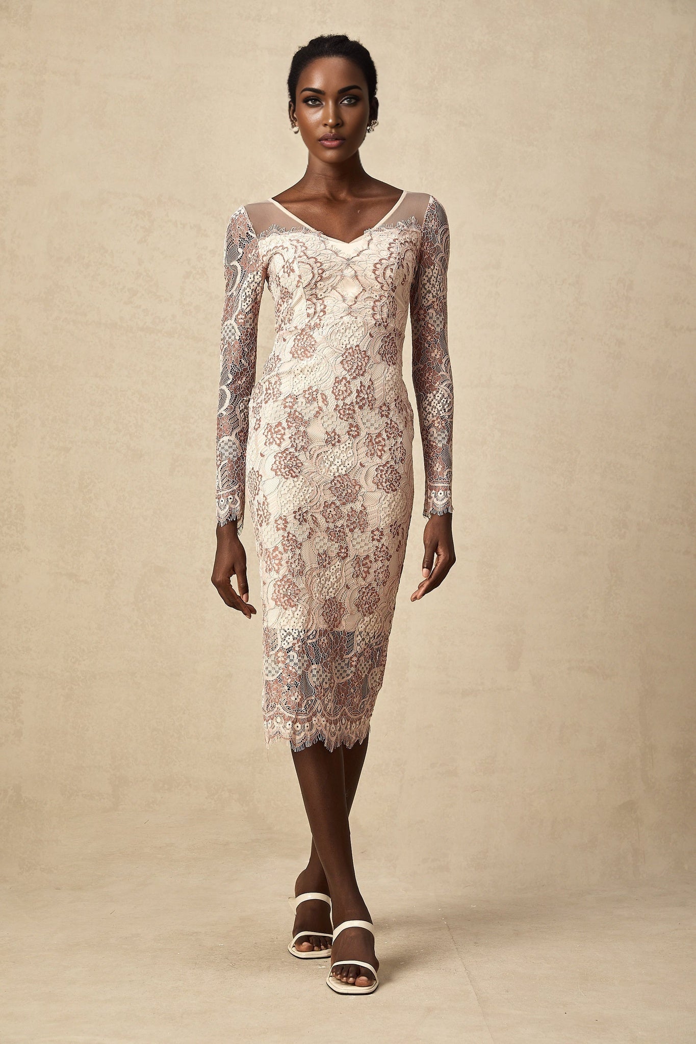 A woman wearing a fitted midi dress made of white guipure lace standing in a neutral background