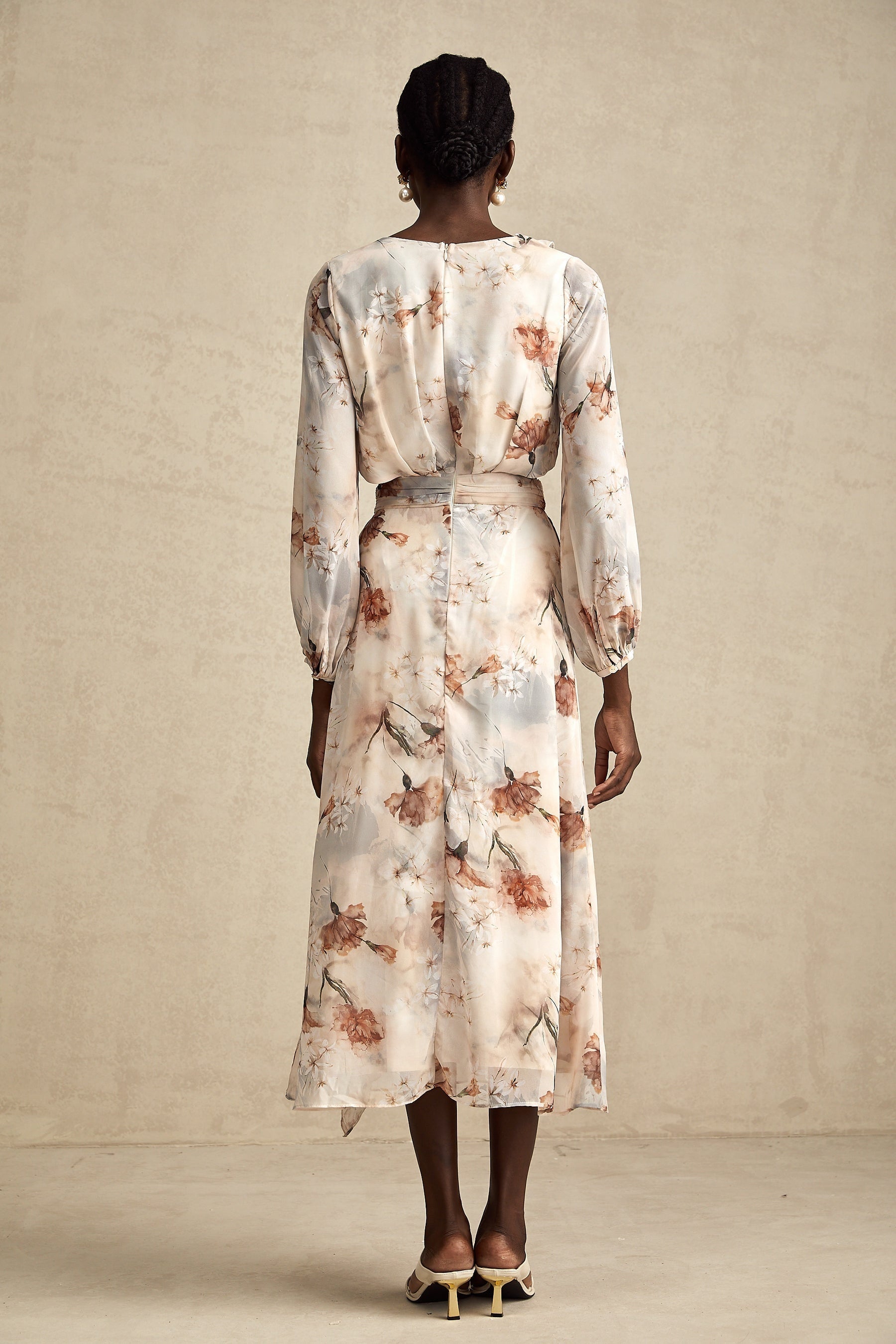 A woman wearing a floral print midi dress with an open waist design The dress has a colorful floral pattern on a light background It features long sleeves and a flowing skirt that falls to mid calf length The open waist detail adds a stylish and flattering touch to the silhouette