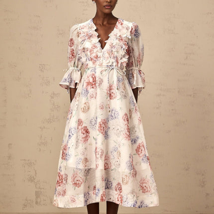 A woman wearing a floral print midi dress with three dimensional petal details on a light colored background