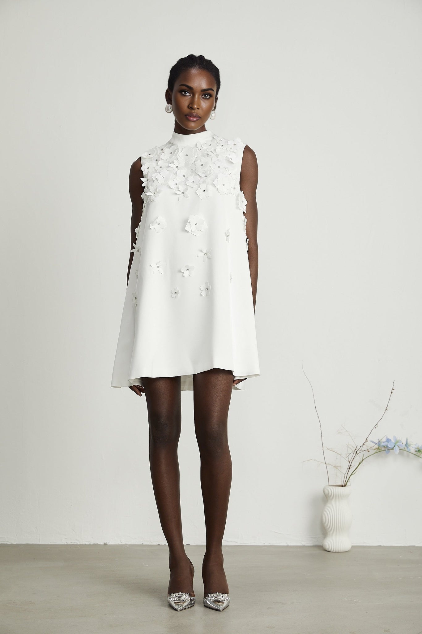 A woman wearing a floral print mini dress with short sleeves and a fitted silhouette standing against a plain background