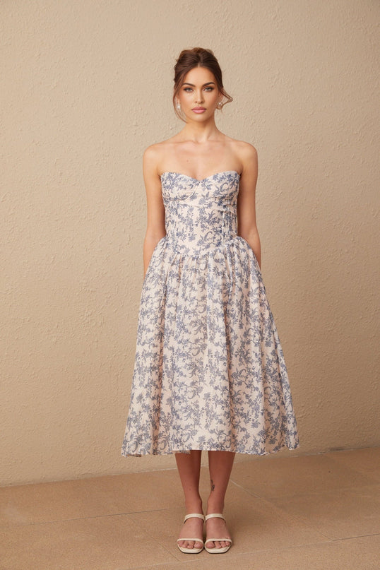 A woman wearing a floral print off shoulder midi dress with a fanny silhouette standing against a plain background