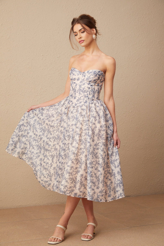 A woman wearing a floral print off shoulder midi dress with a fitted bodice and flared skirt standing against a plain background
