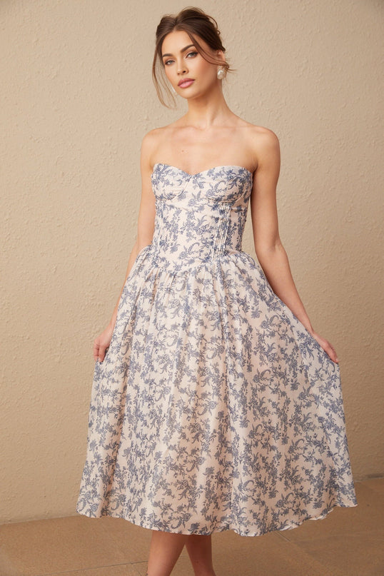 A woman wearing a floral print off shoulder midi dress with a fitted bodice and flowy skirt standing in a casual pose
