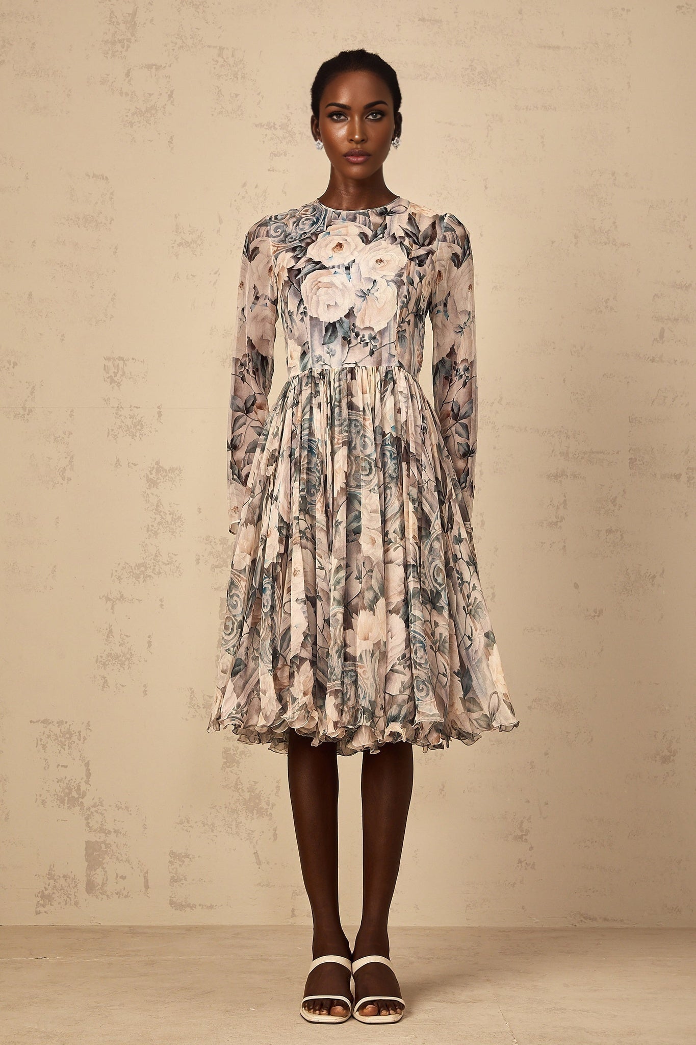 A woman wearing a floral print pleated chiffon midi dress with a flowing skirt and delicate pattern standing in a casual pose against a plain background