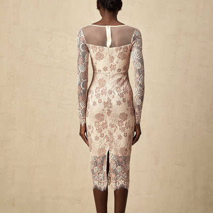 A woman wearing a formfitting midi dress made of white guipure lace with intricate floral patterns standing against a plain background