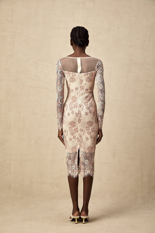 A woman wearing a formfitting midi dress made of white guipure lace with intricate floral patterns standing against a plain background