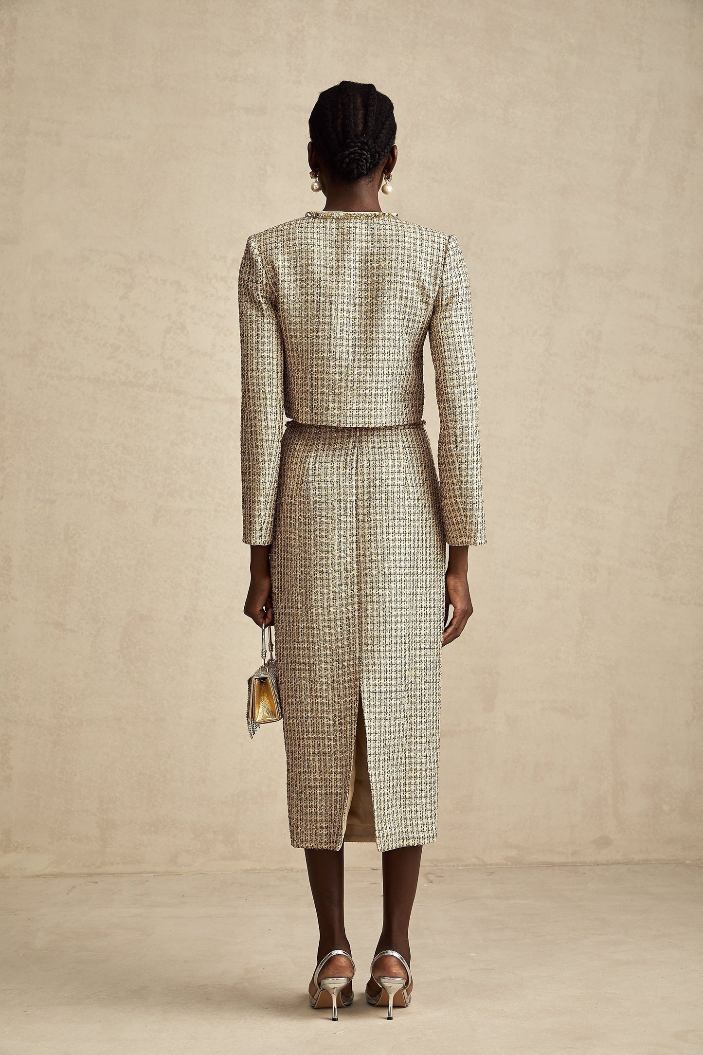 A woman wearing a gold tweed jacket and matching skirt set adorned with sequins The outfit has a luxurious and sparkling appearance suitable for formal or evening events