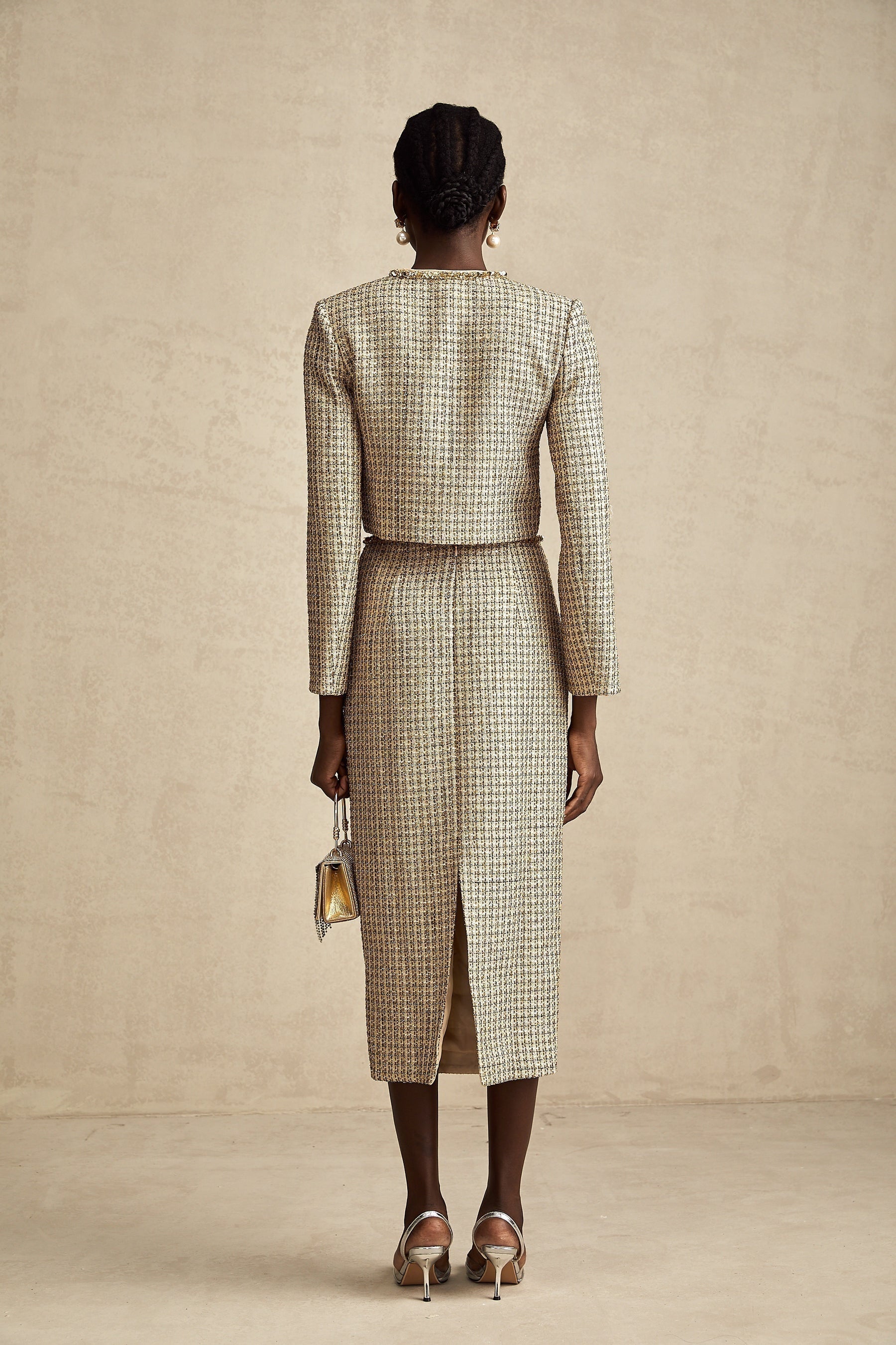 A woman wearing a gold tweed jacket and matching skirt set adorned with sequins The outfit has a luxurious and sparkling appearance suitable for formal or evening events