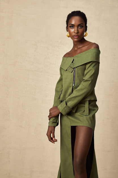 A woman wearing a green asymmetric jacket paired with a matching skirt standing against a plain background