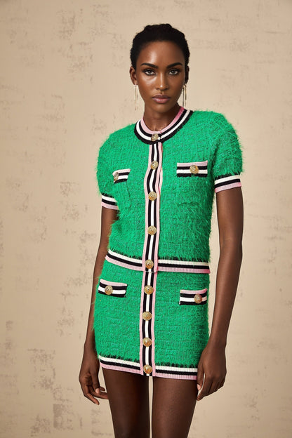 A woman wearing a green knitted matching set consisting of a top and skirt standing against a plain background