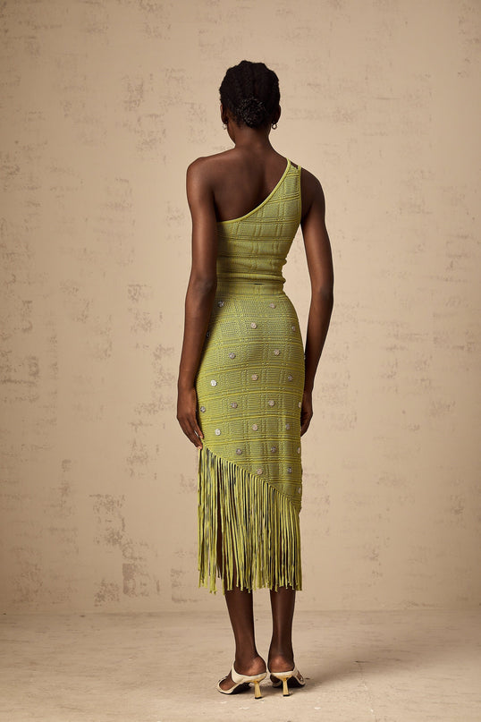 A woman wearing a green knitted two piece outfit consisting of a sleeveless top and matching skirt The top features embellishments and the set has a fitted silhouette