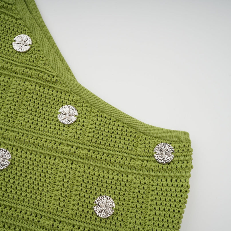 A woman wearing a green knitted two piece outfit consisting of a sleeveless top and matching skirt with embellished details