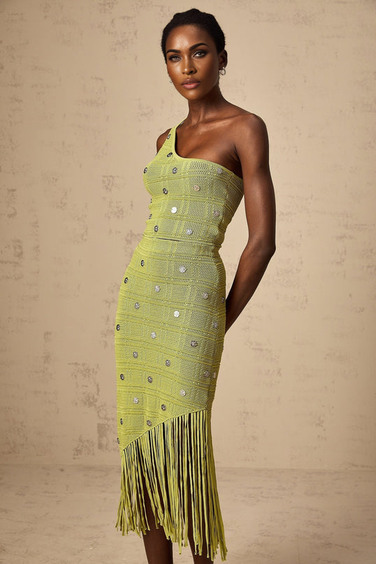 A woman wearing a green knitted two piece outfit consisting of a top and skirt with embellishments The set has a matching design and is called Annette