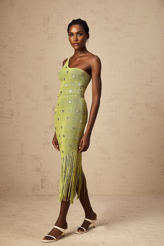 A woman wearing a green knitted two piece outfit consisting of a top and skirt with embellishments The top is sleeveless and the skirt is knee length Both pieces feature decorative beading or sequins