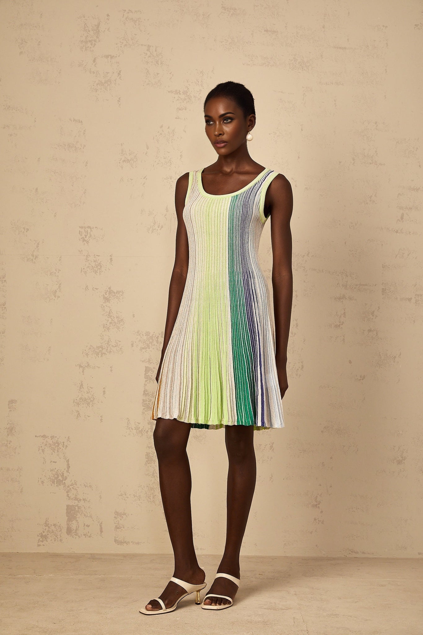 A woman wearing a green mini dress with horizontal sequin stripes and knit fabric standing in a neutral pose