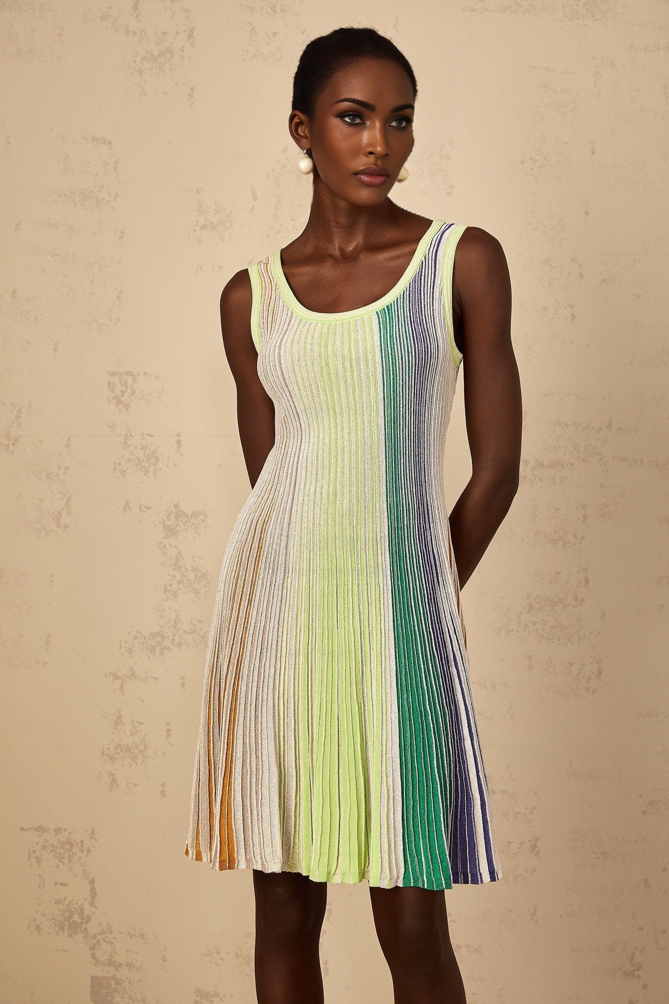 A woman wearing a green mini dress with sequin stripes and a knit texture standing against a plain background
