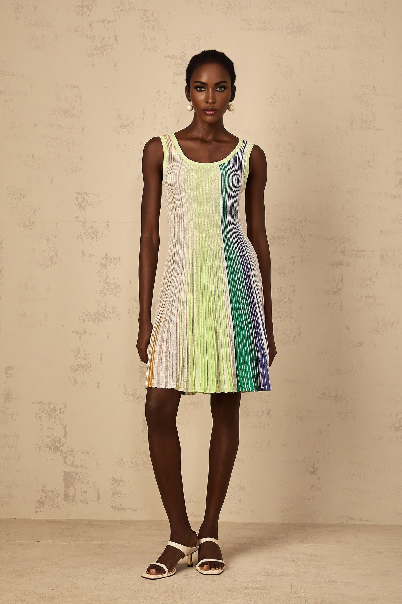A woman wearing a green mini dress with sequin stripes and a knit texture standing against a plain background