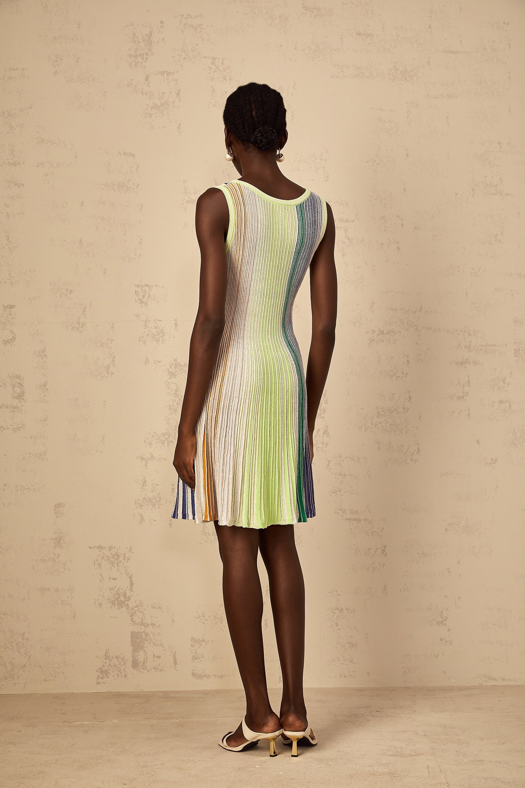 A woman wearing a green mini dress with sequin stripes knitted into the fabric the dress has a close fitting silhouette and short length